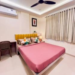 Modern bedroom with double bed, air conditioner, study desk, and cozy interior in a fully furnished service apartment