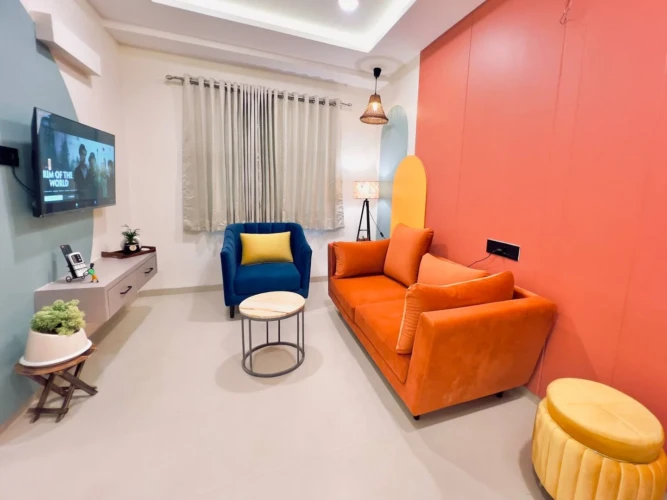 Modern living room with orange sofa, blue armchair, wall-mounted TV, and stylish decor in a fully furnished service apartment for corporates
