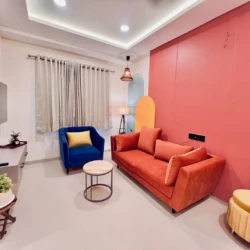 Modern living room with orange sofa, blue armchair, wall-mounted TV, and stylish decor in a fully furnished service apartment for corporates