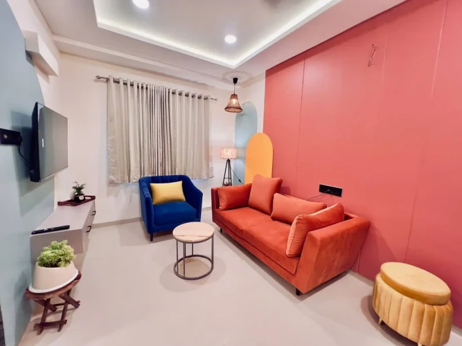 Modern living room with orange sofa, blue armchair, wall-mounted TV, and stylish decor in a fully furnished service apartment for corporates