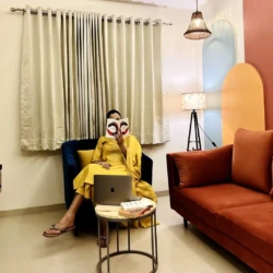 Woman reading book while sitting on a modern blue armchair in a fully furnished living room of service apartment for coporates